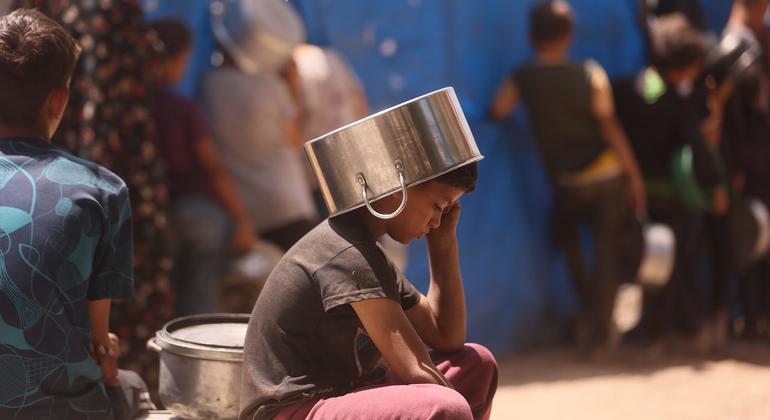 Un niño se pone una olla en la cabeza para protegerse del sol mientras espera para comer.